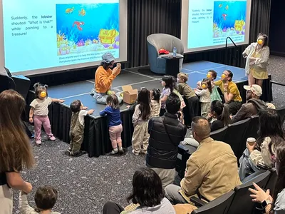 Karla interacting with a group of children during a storytelling performance. An animated underwater and fun scene is projected on screens behind her.